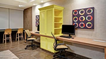 A conference room with a yellow cabinet, two chairs, a desk with a computer, and a wall-mounted monitor.