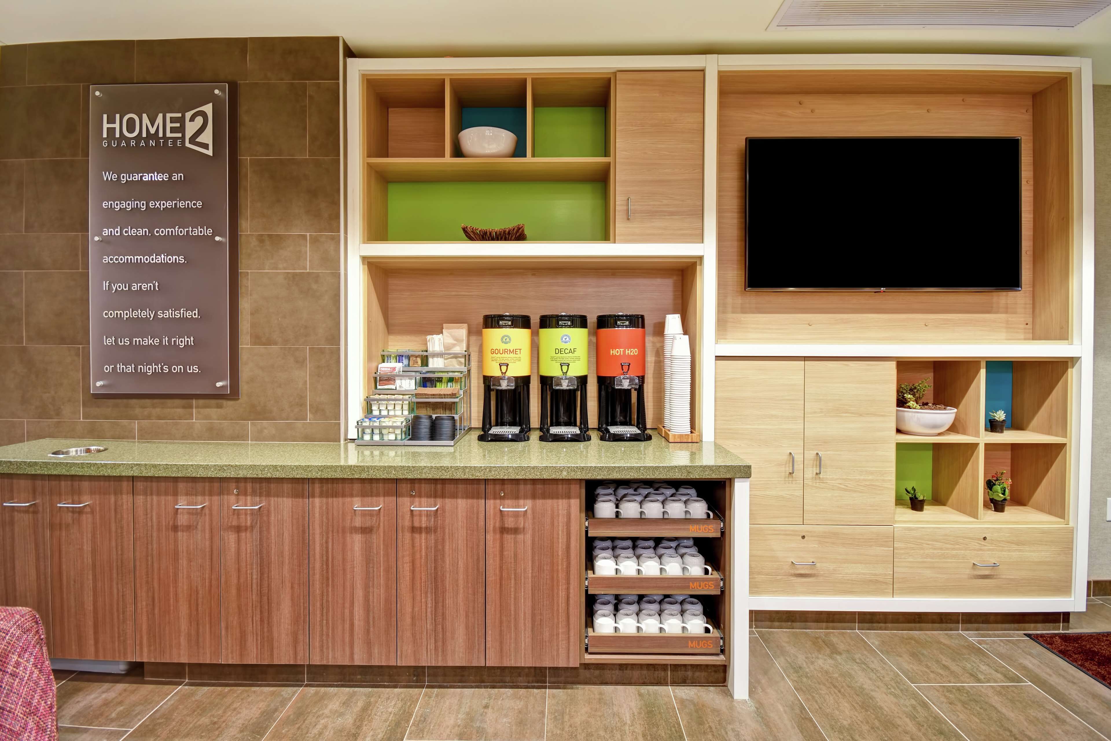 A modern kitchen with a coffee station, a TV, and a sign about a home guarantee.