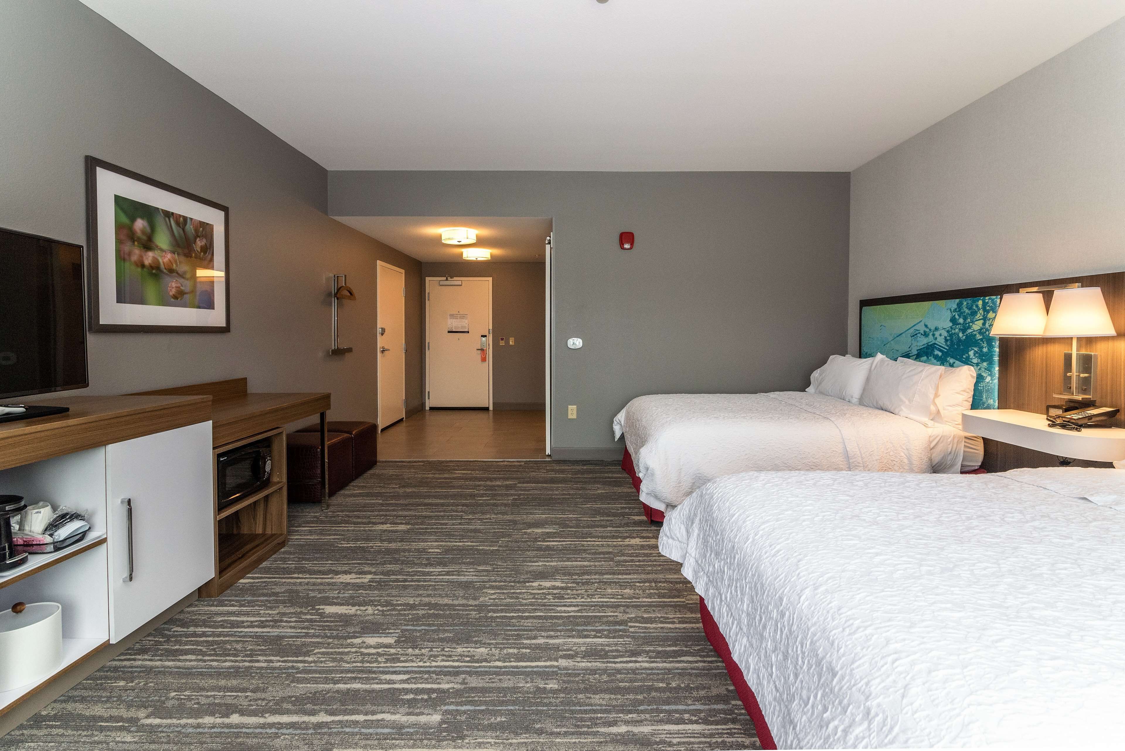 A hotel room with two beds, a desk, a TV, and a painting on the wall.