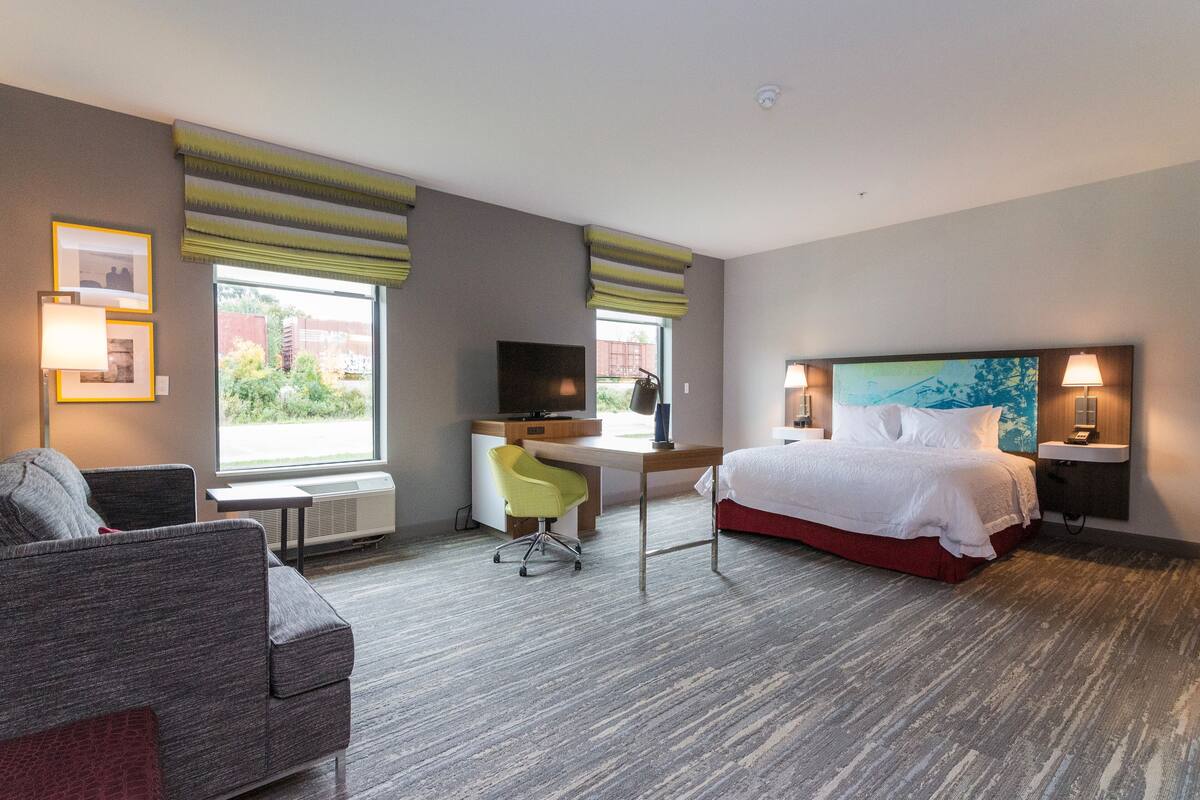 Une chambre d’hôtel avec un lit, un bureau, une chaise et une grande fenêtre.