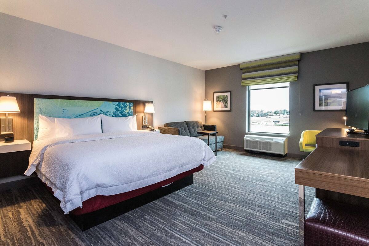 Une chambre d’hôtel avec un grand lit, un bureau, une chaise, une télévision et une fenêtre donnant sur un beau paysage.