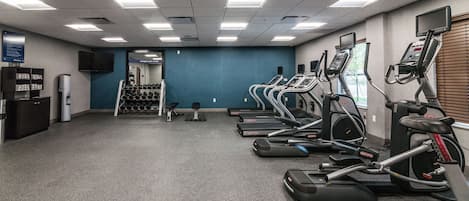 A gym with treadmills, dumbbells, and a television on the wall.