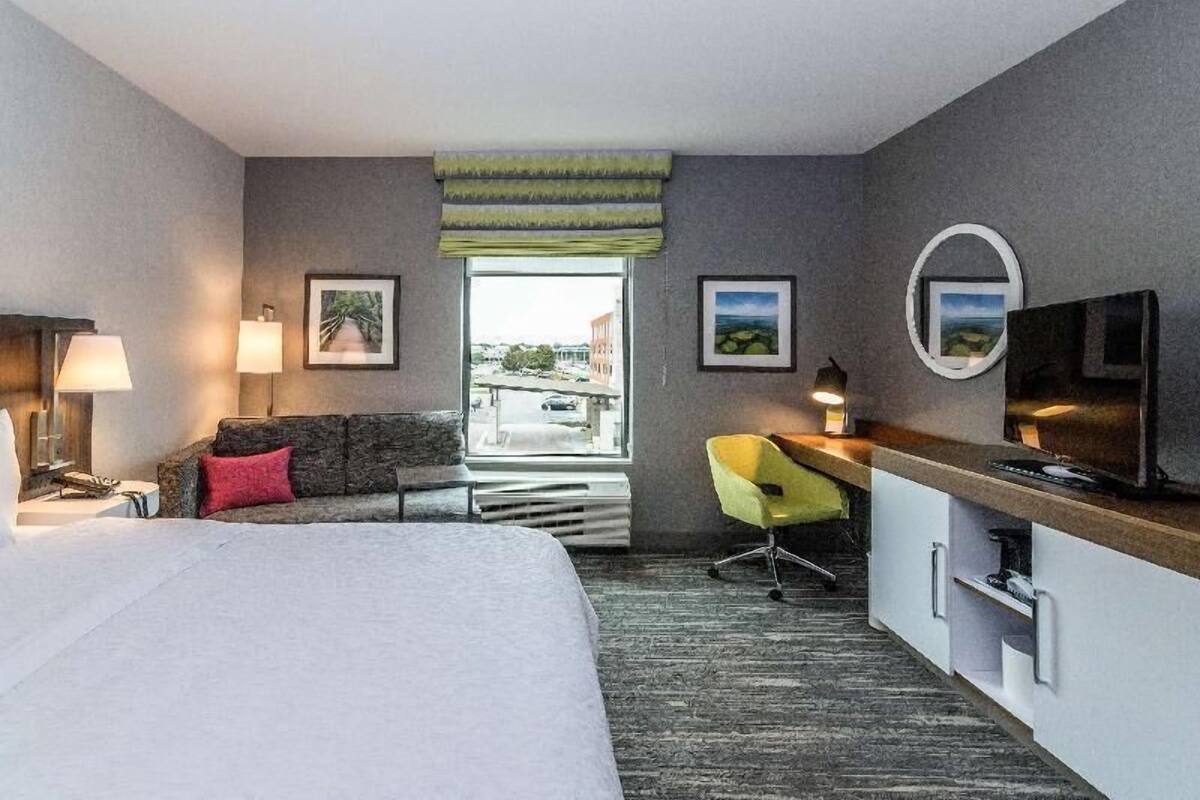 Une chambre d’hôtel équipée d’un lit, d’un bureau, d’une chaise, d’une télévision et d’une fenêtre donnant sur un paysage agréable.