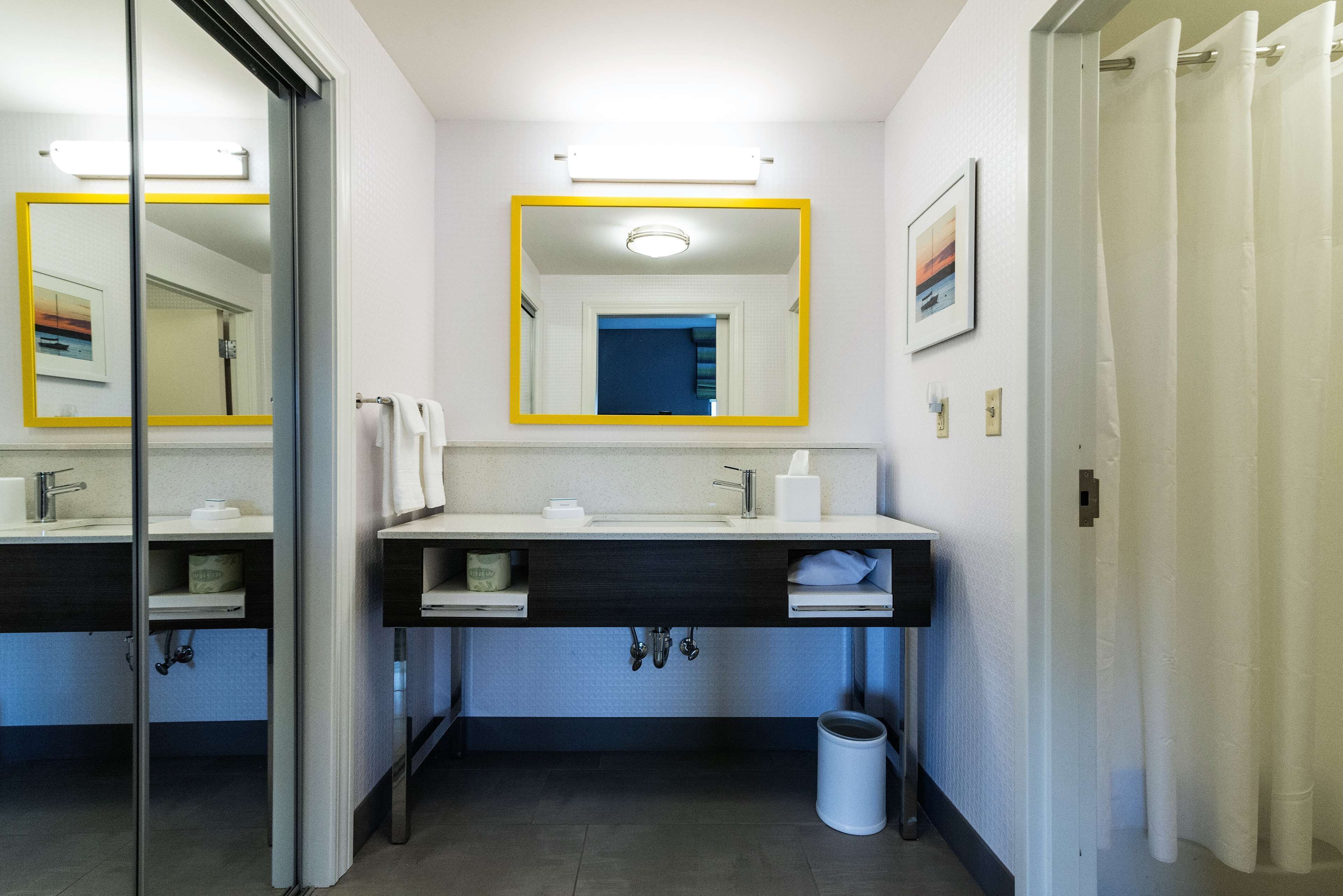 A modern bathroom with two sinks, a mirror, and a trash can.