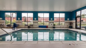 An indoor swimming pool with clear windows, a blue wall, and a view of a train yard. - Hampton Inn & Suites Allen Park (Allen Park)