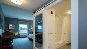 A hotel room with a bed, a desk, a chair, a shower, and a bathroom. - Hampton Inn & Suites Allen Park (Allen Park)