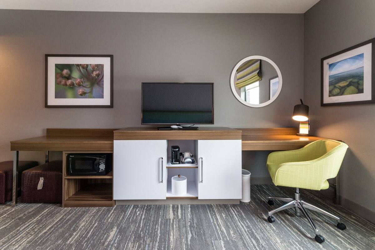 Une chambre d’hôtel moderne équipée d’un téléviseur à écran plat, d’un bureau avec un ordinateur, d’une chaise et d’un four à micro-ondes.