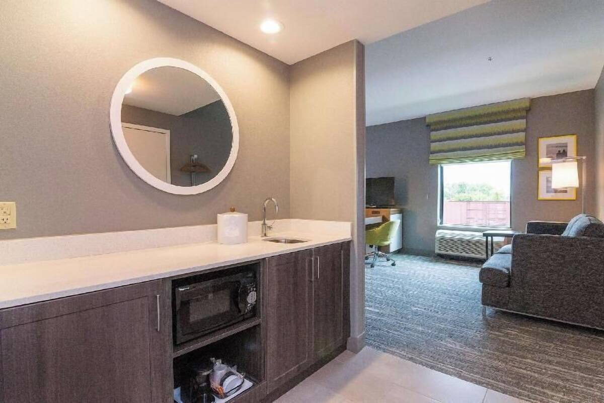 Une salle de bain moderne avec un miroir rond, un lavabo et des meubles de rangement de couleur sombre.