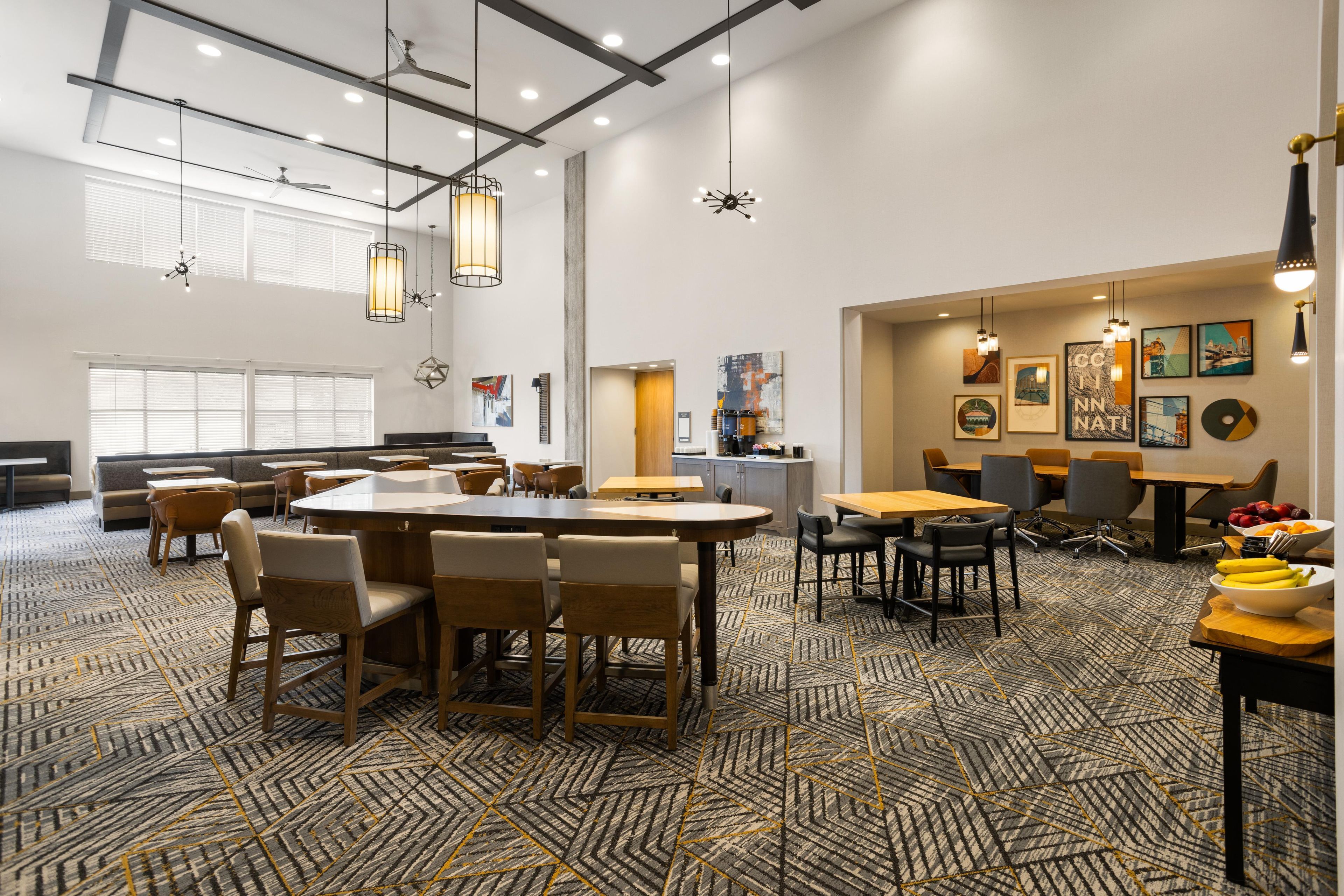 Een ruime eetzaal van een hotel met meerdere tafels en stoelen, een keukenhoek en kunstwerken aan de muren.