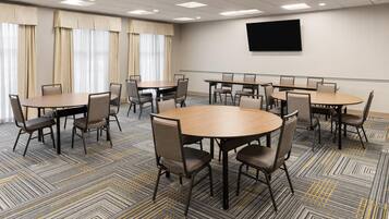 A conference room with multiple tables and chairs, a flat-screen TV on the wall, and large windows with curtains.