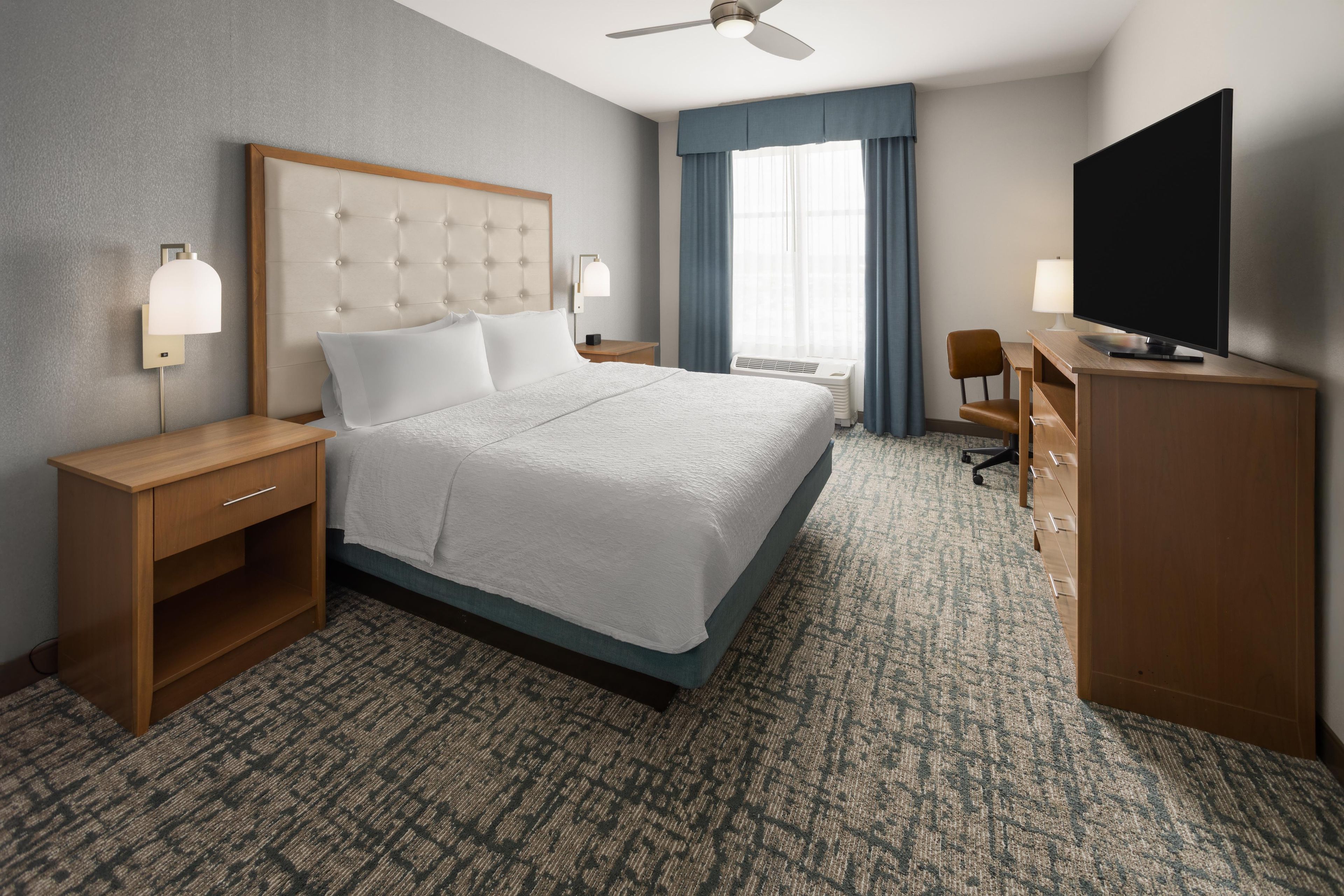 A hotel room with a large bed, a desk, a chair, a television, and a ceiling fan.