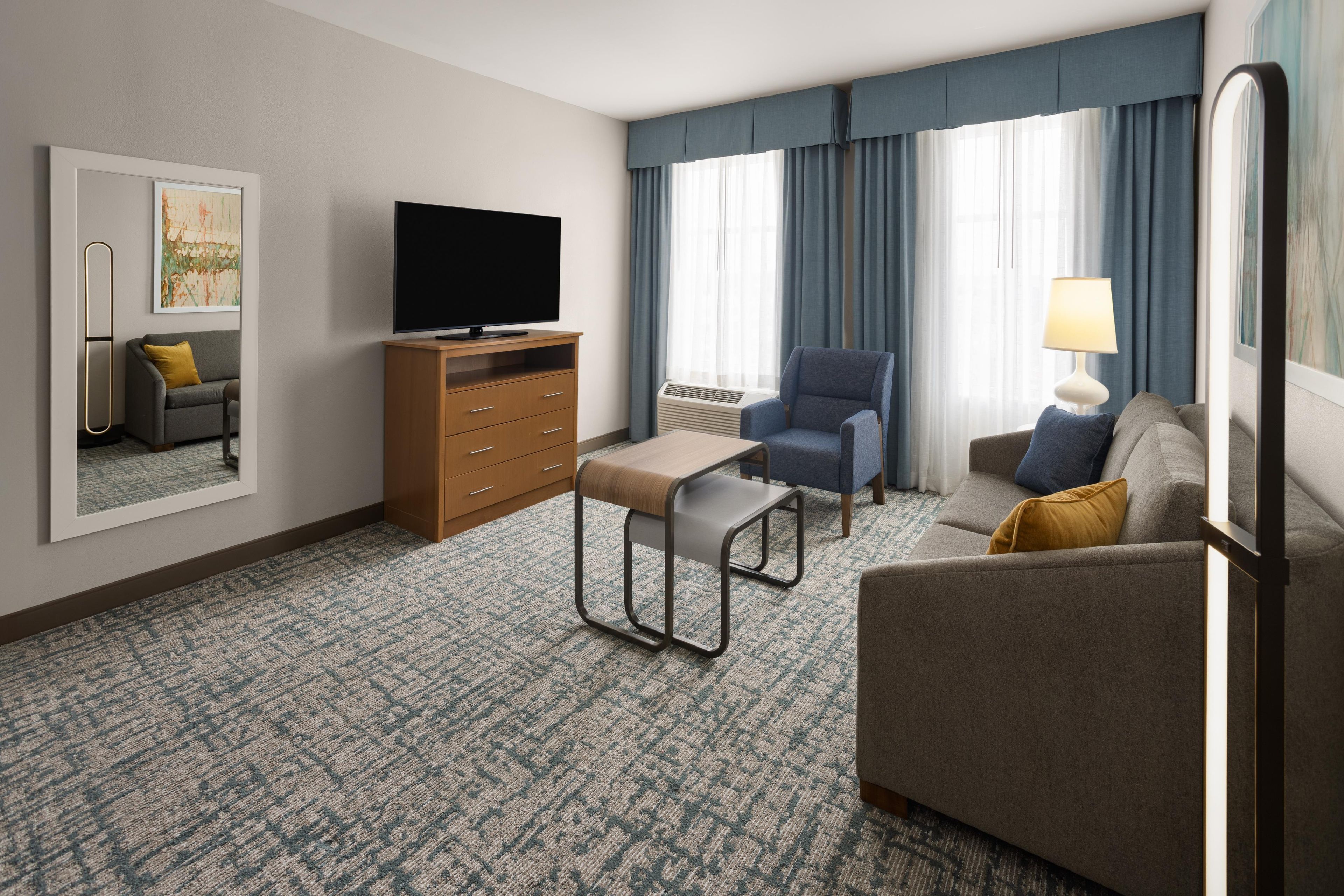 Habitación de hotel con televisión de pantalla plana, sofá, sillón, mesita, cómoda y lámpara.
