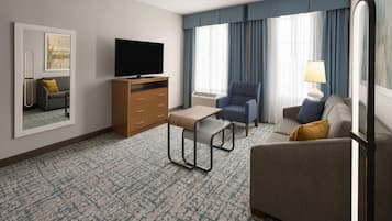 Habitación de hotel con televisión de pantalla plana, sofá, sillón, mesita, cómoda y lámpara.