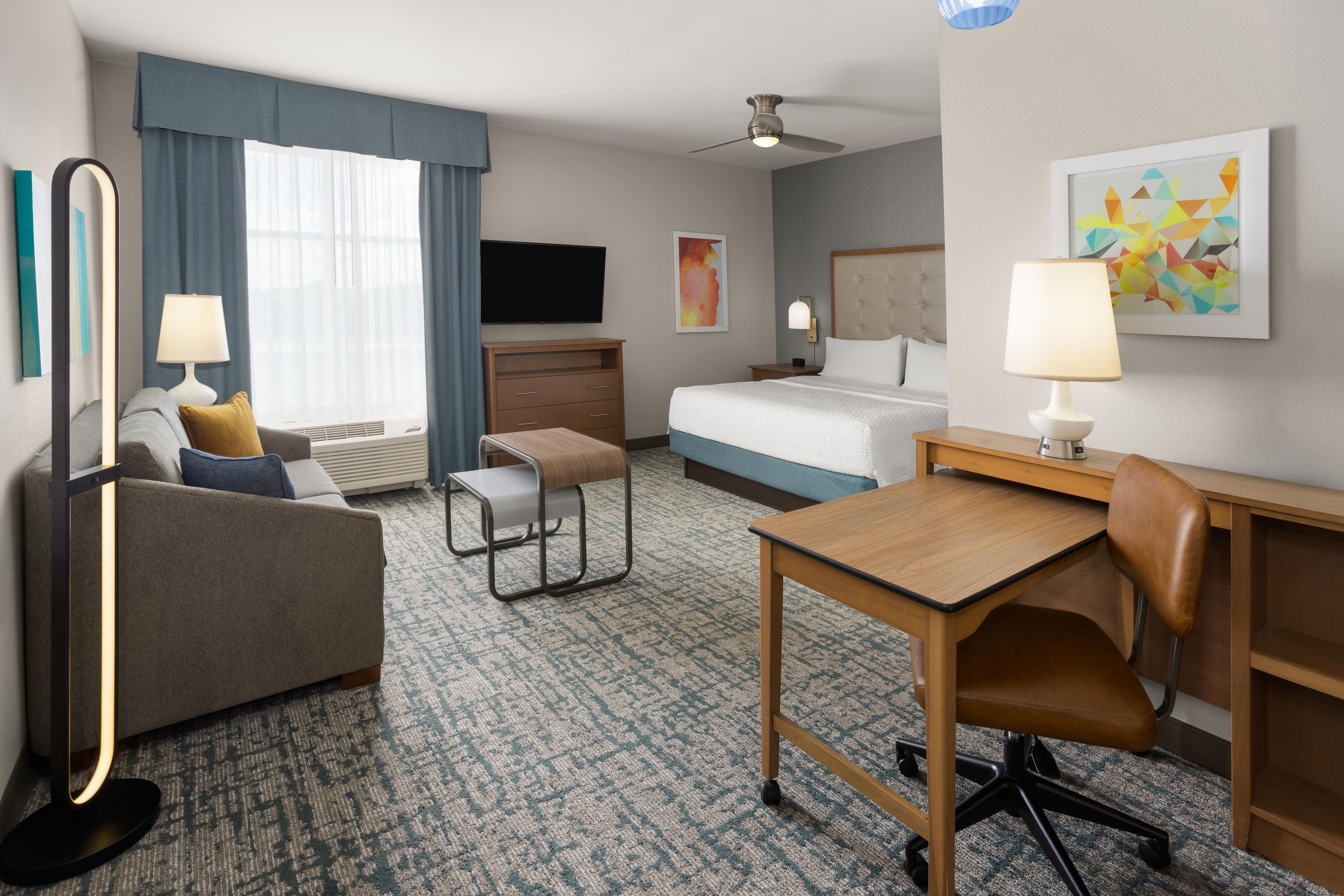 A hotel room with a bed, desk, chair, sofa, and a television.