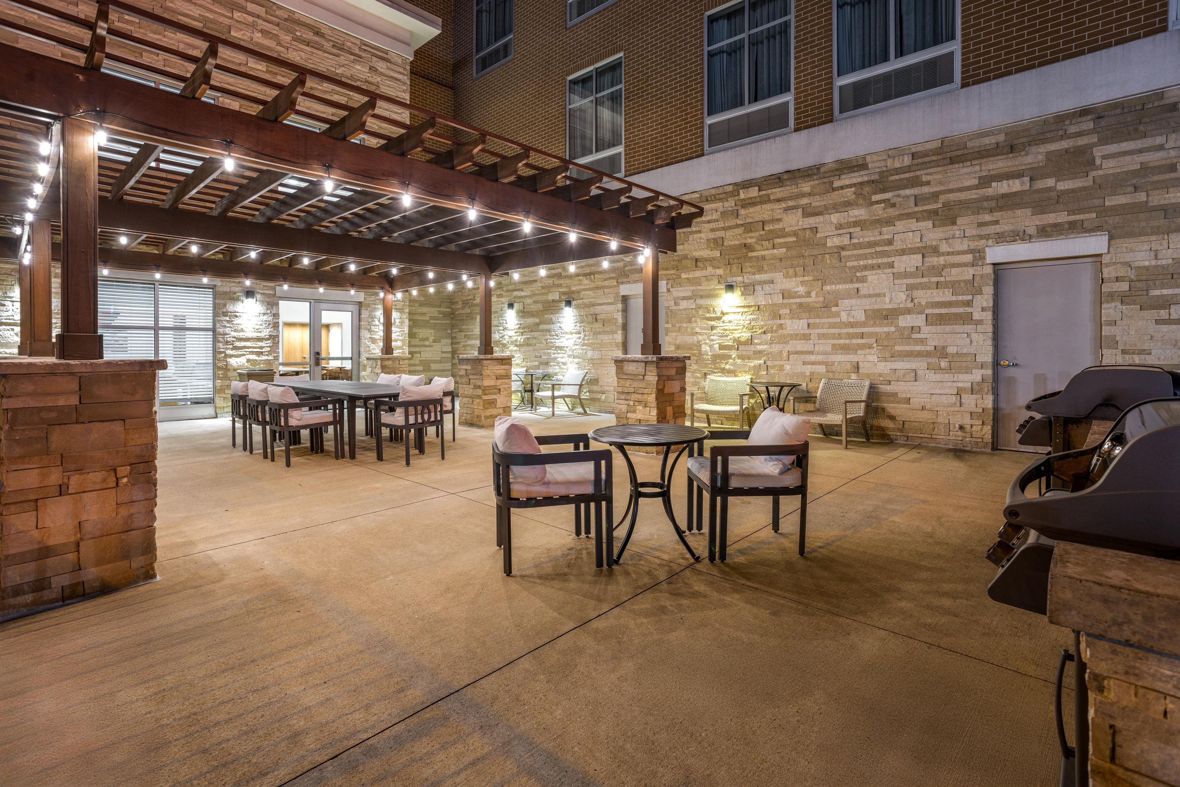 Un patio al aire libre con paredes de piedra, mobiliario de madera y luces colgantes.
