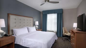 A hotel room with a large bed, two bedside tables with lamps, a desk with a television, a chair, and a ceiling fan.
