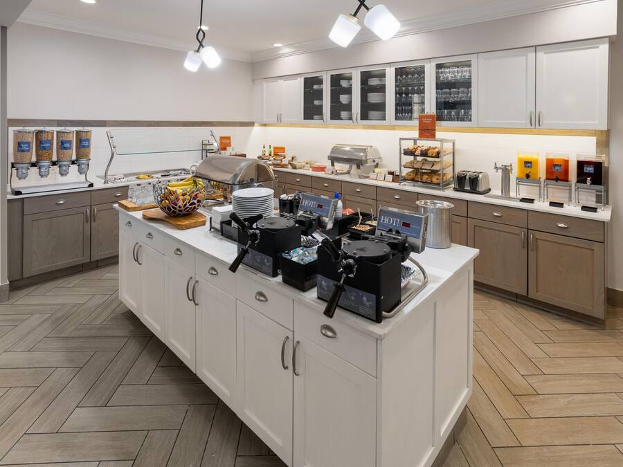 Cuina moderna amb una illa central, equipada amb màquines de cafè, expositor d'aliments i zona de begudes.