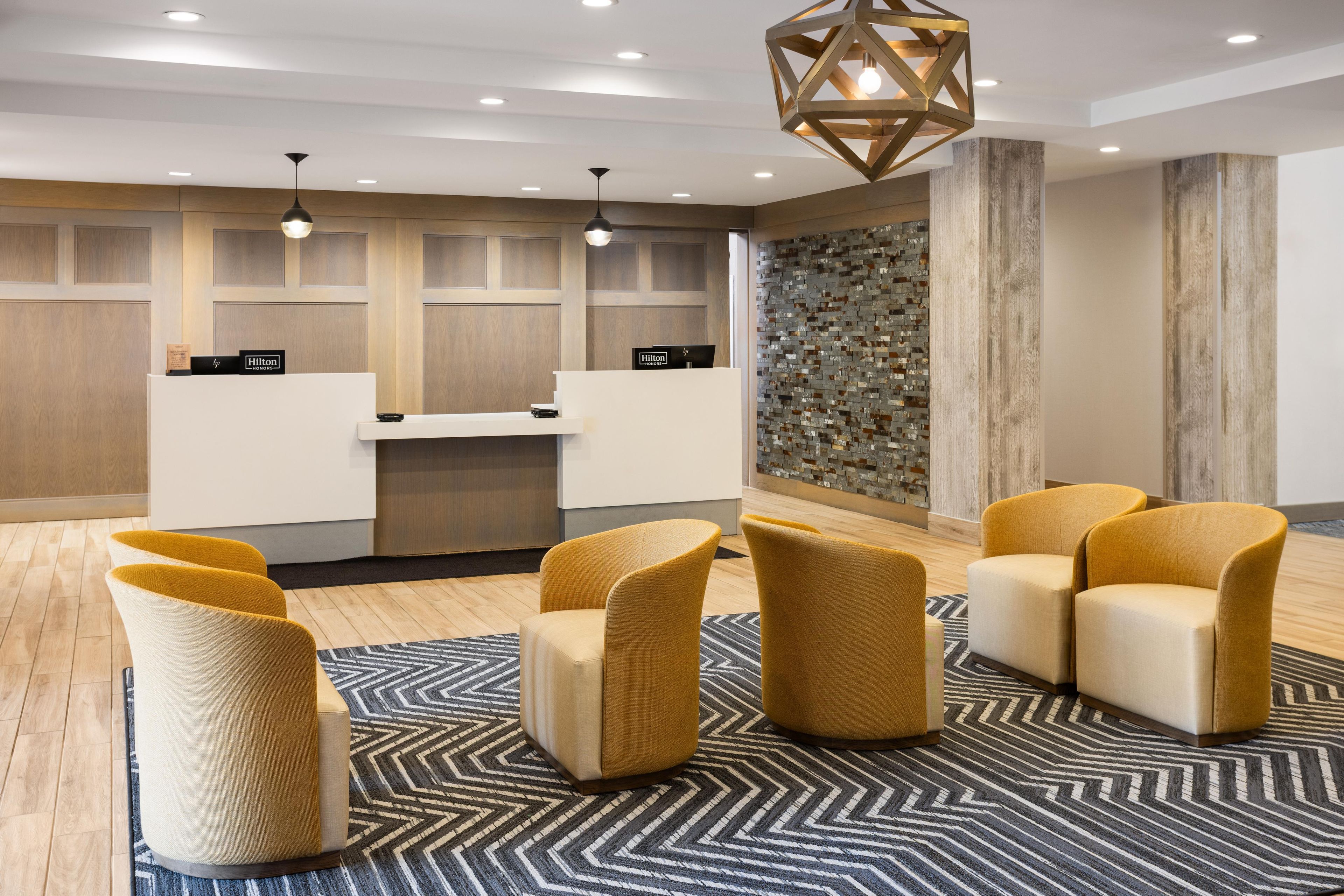 A hotel reception area with a modern design, featuring a reception desk, seating area with chairs, and a decorative wall.