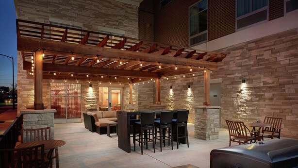 Un patio al aire libre con una pérgola de madera, muros de piedra y una parrilla.