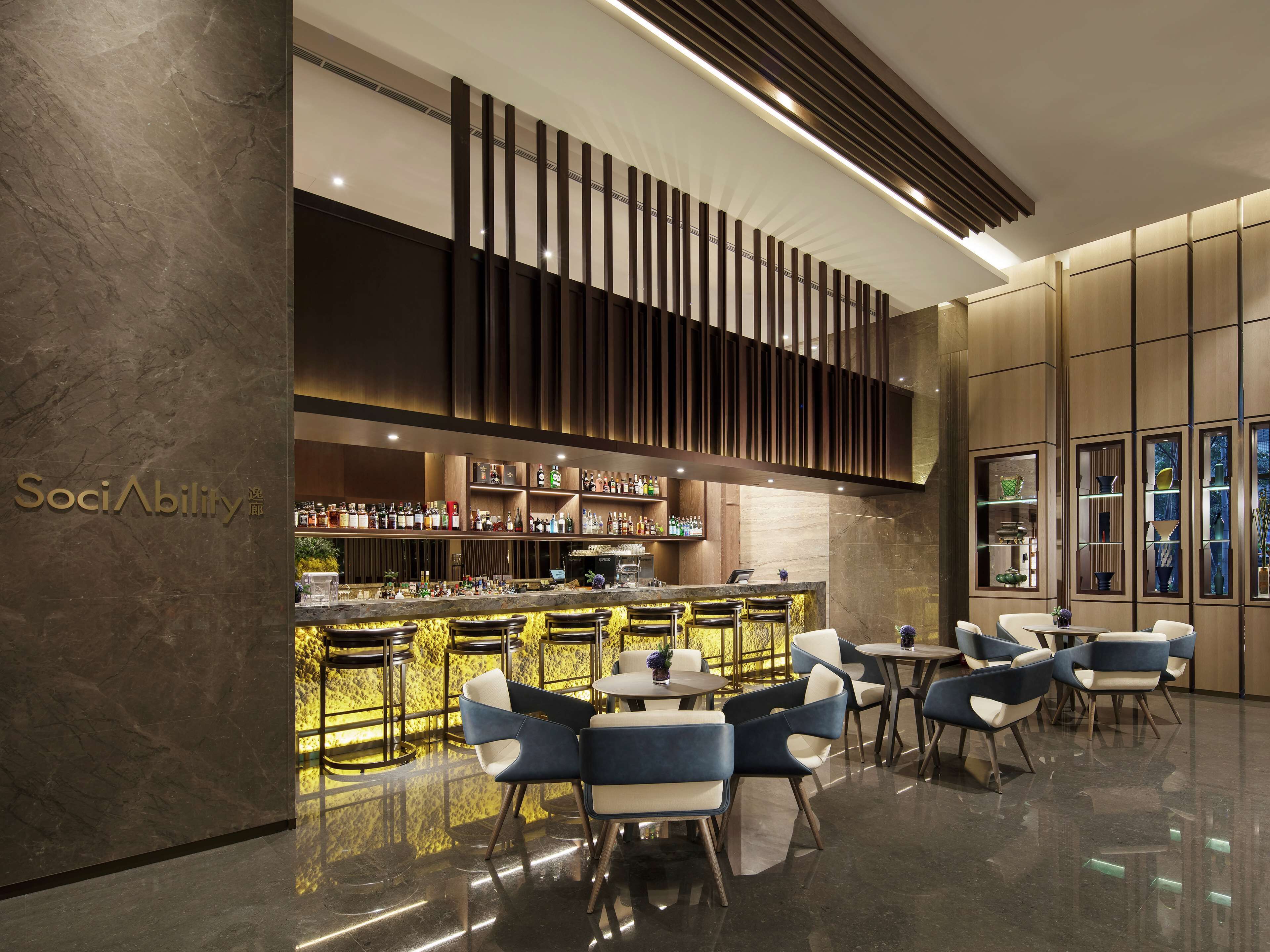 A modern bar area with a polished marble floor, a variety of seating options including bar stools and tables, and a well-stocked bar with numerous bottles and glasses.
