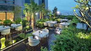 A rooftop garden with outdoor seating, a pond, and a city view. - Hilton Taipei Sinban (New Taipei City)