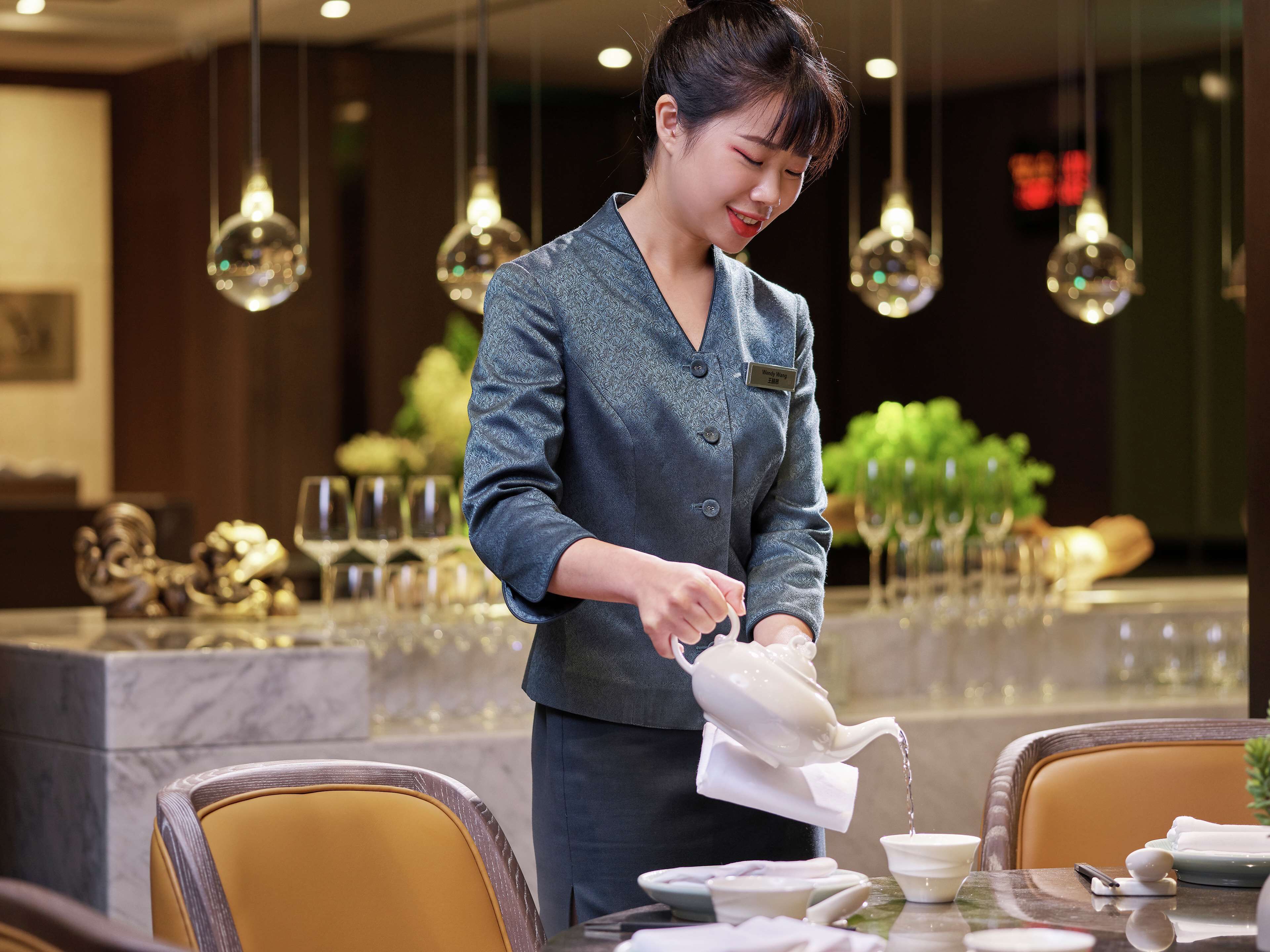 A person pouring water into a teapot at a table in a restaurant setting.