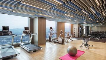 A modern gym with treadmills, stationary bikes, and exercise balls, featuring large windows and a wooden floor.
