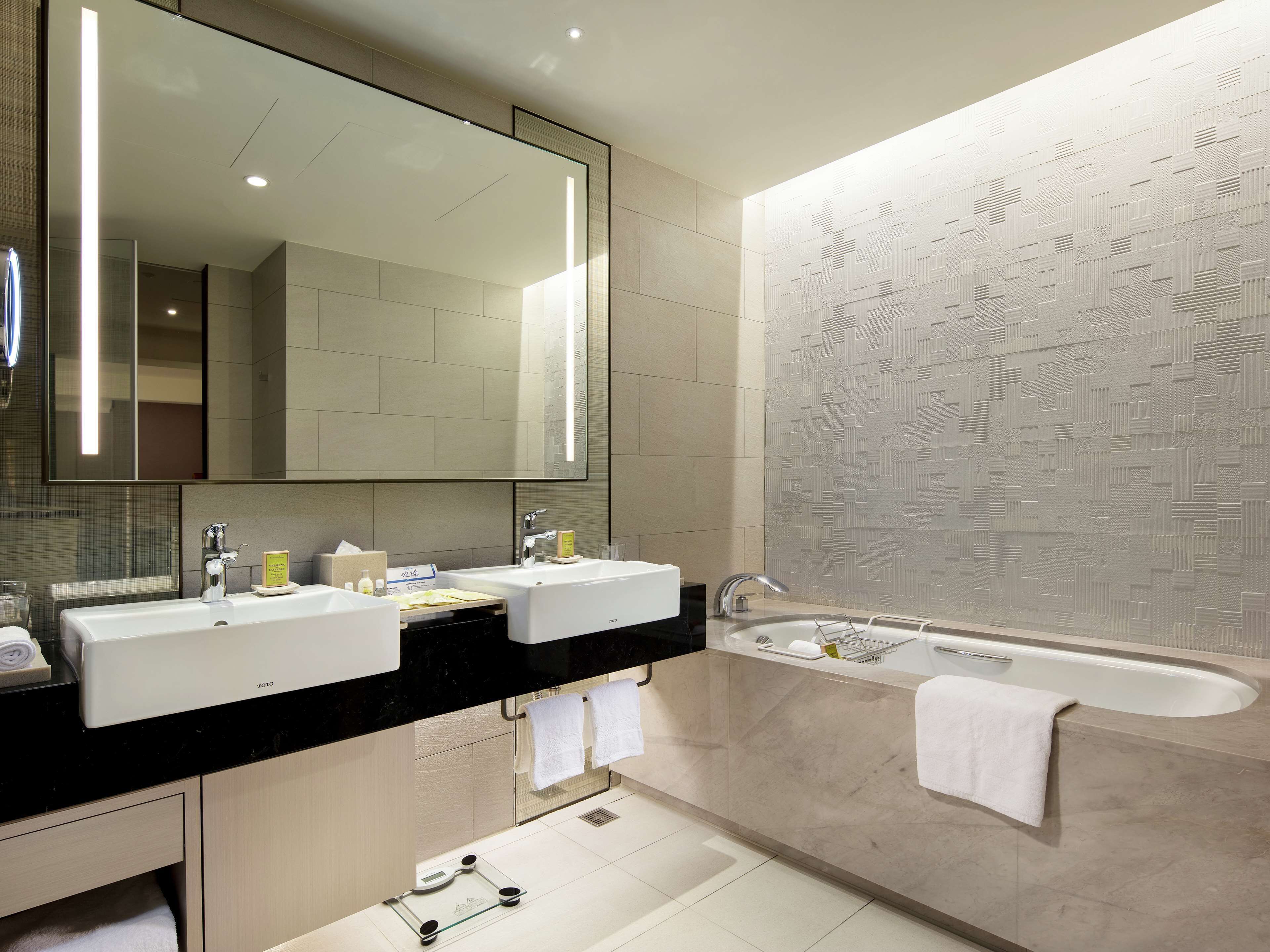A modern bathroom with two sinks, a large mirror, and a bathtub.
