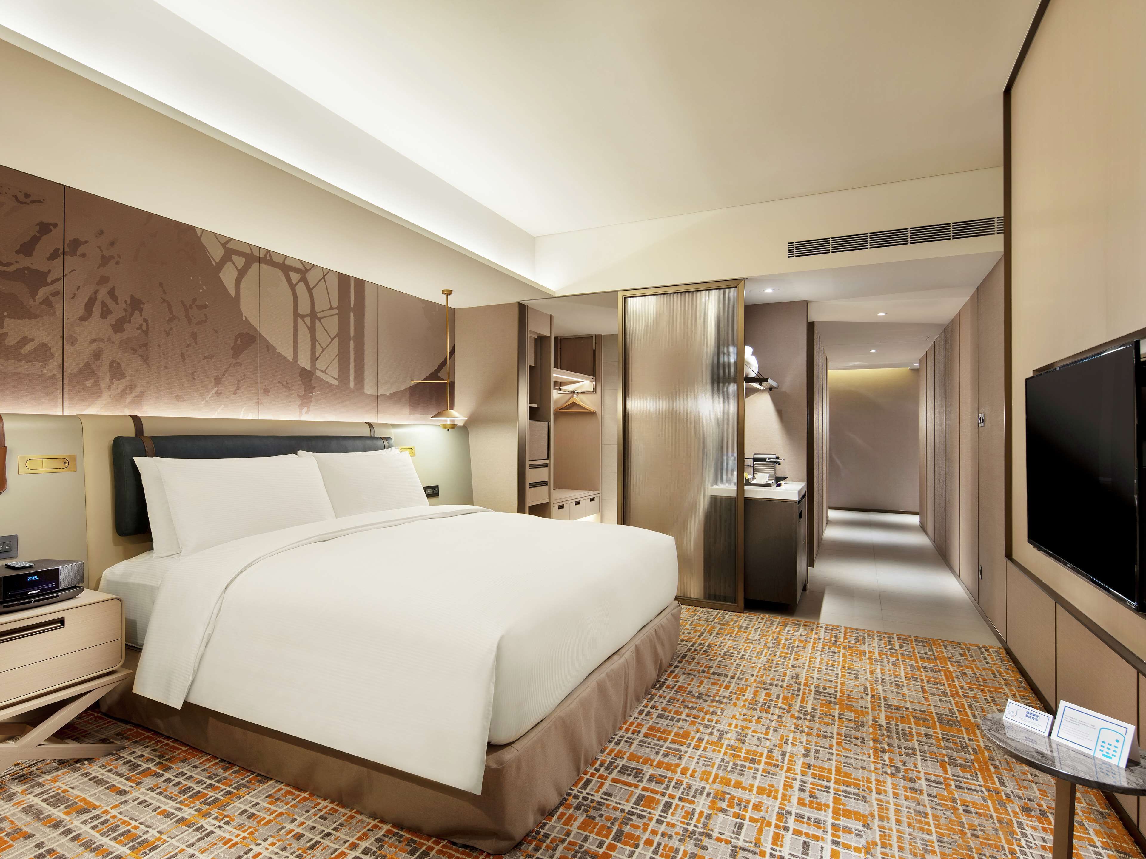 A hotel room with a large bed, bedside table, TV, and a bathroom with a shower and toilet.
