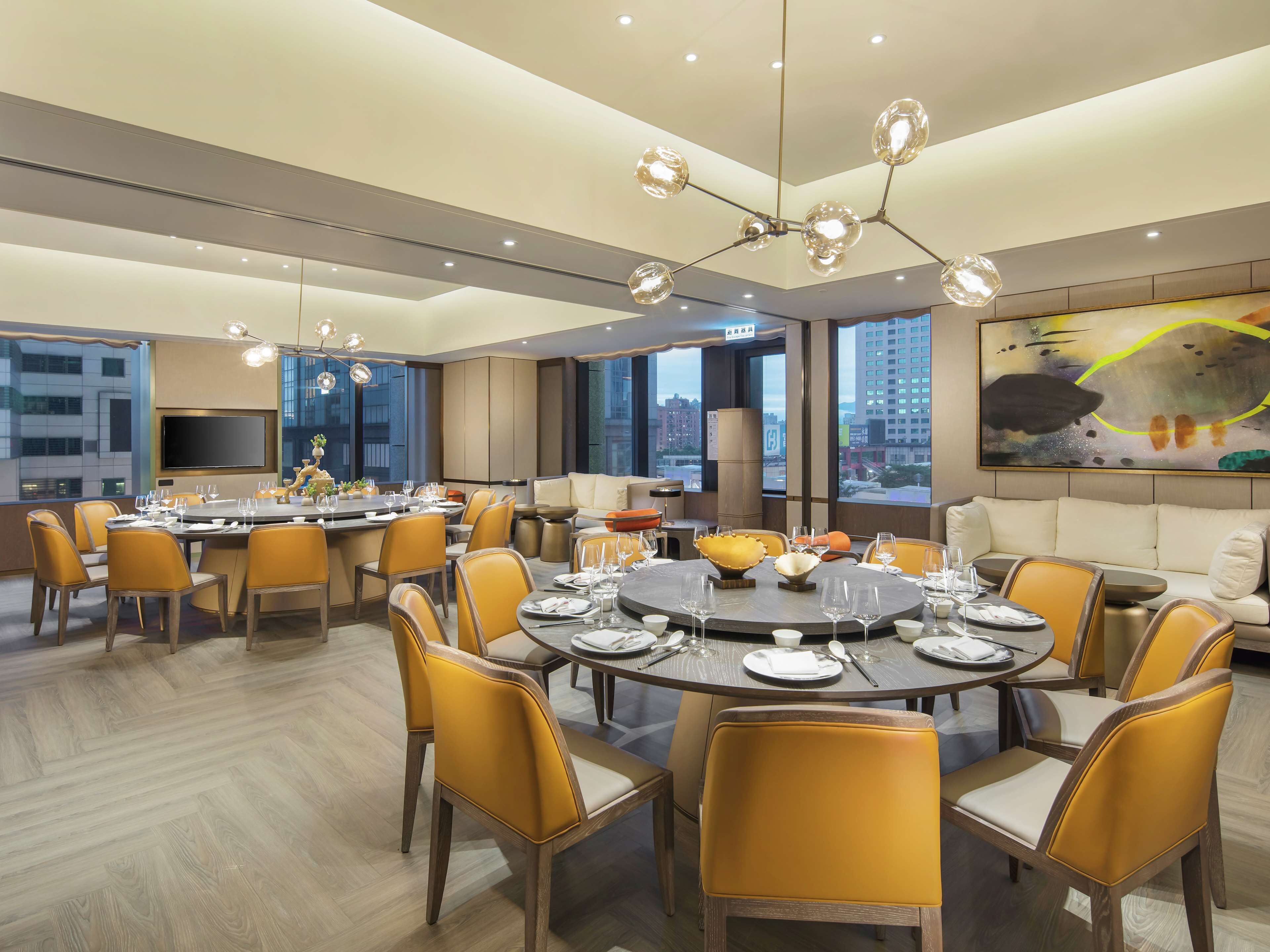 A modern dining area with round tables, yellow chairs, and a large painting on the wall.
