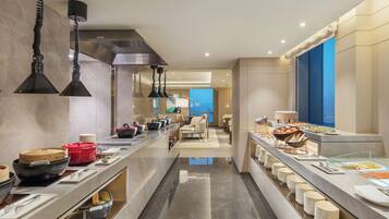 Un bufé moderno de hotel con una larga barra, diversos alimentos y vistas al mar.