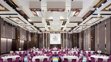 A large conference room with round tables, purple chairs, and a central screen displaying the Hilton logo.