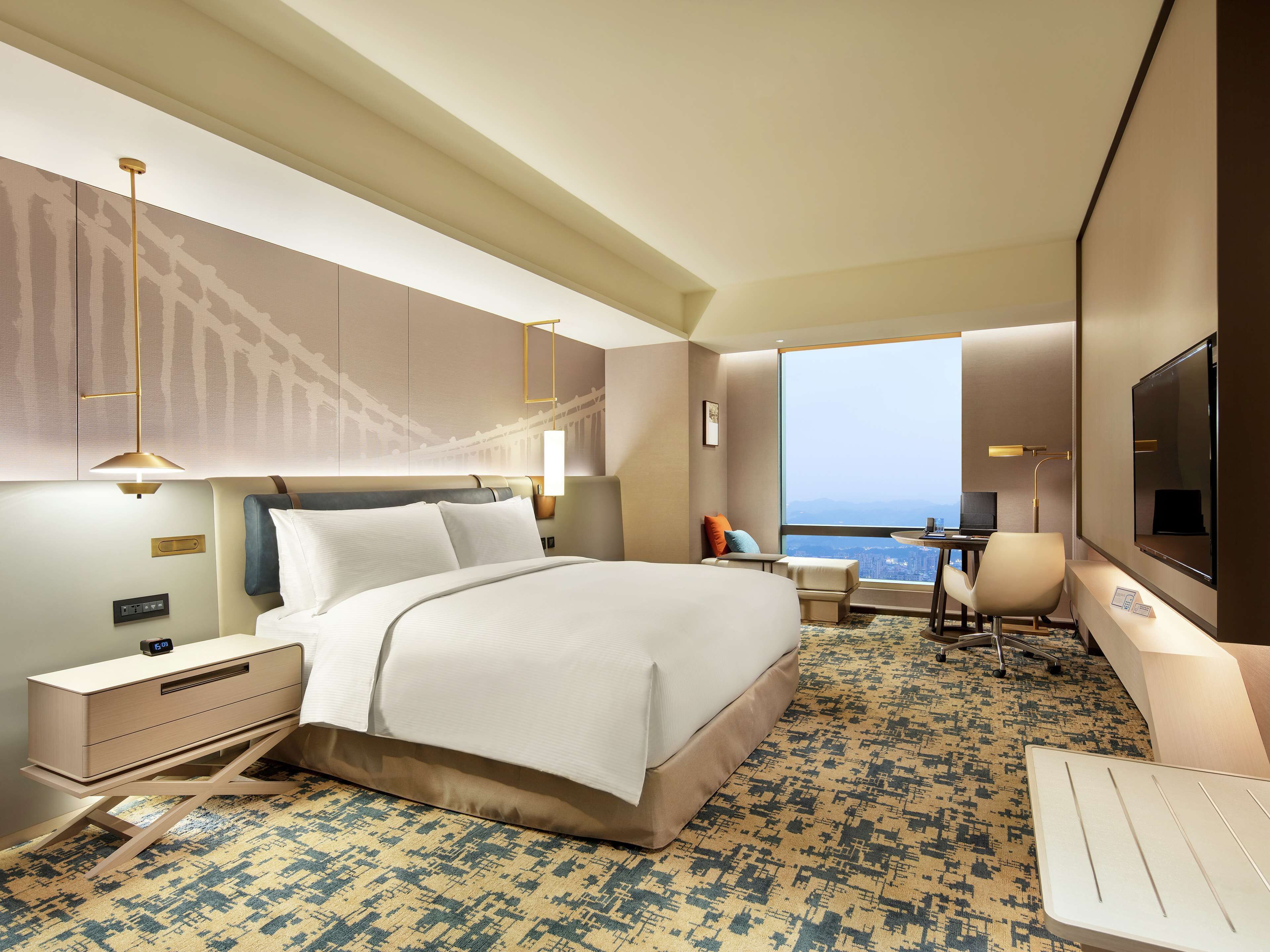 Una habitación de hotel moderna con una cama grande, un escritorio, una silla y vistas a la ciudad.