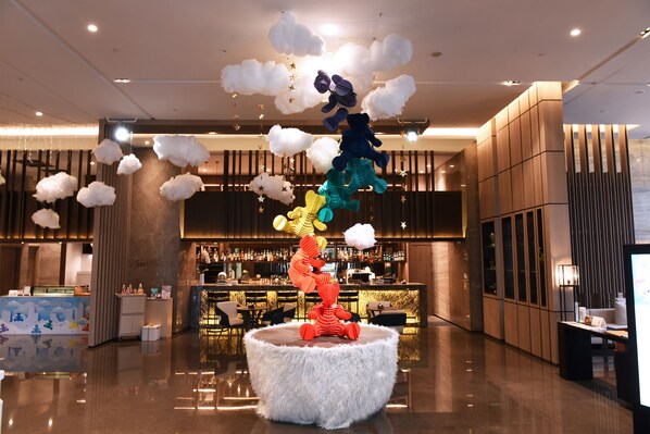Un vestíbulo moderno con una zona de estar central que destaca por una escultura única, un bar con diversas botellas y un suelo pulido.