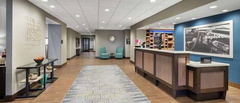 A hotel lobby with a reception desk, seating area, and a large rug with a geometric pattern.
