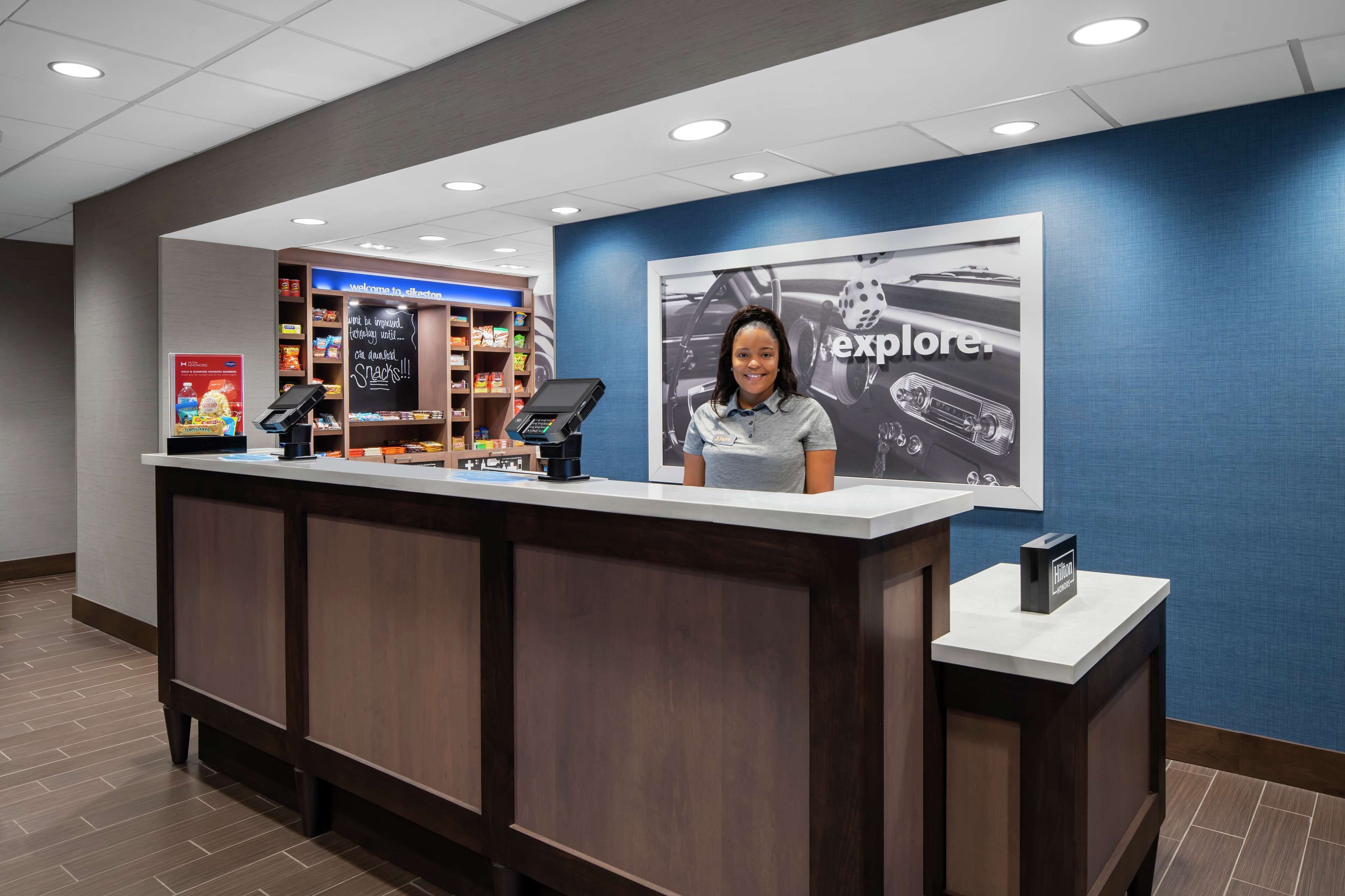 A reception desk with a digital kiosk, a snack display, and a large 'explore' poster on the wall.