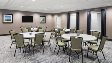 Une salle de conférence équipée de tables et de chaises rondes, d’un téléviseur à écran plat et de tableaux encadrés aux murs.