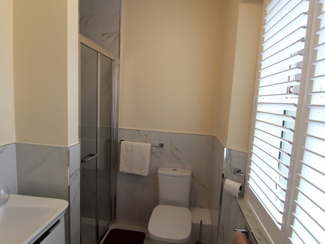 A bathroom with a glass shower enclosure, a toilet, and a window with blinds.
