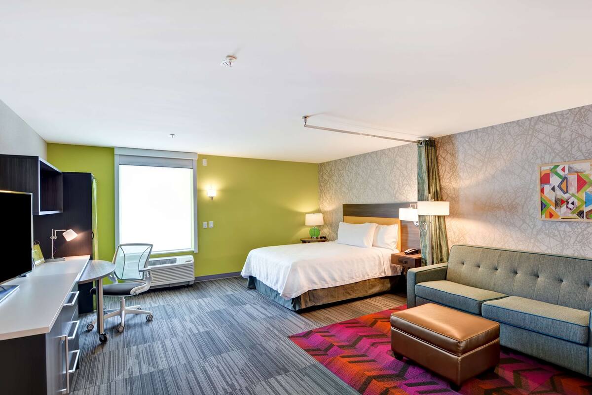 A hotel room with a bed, a sofa, a desk, and a chair.
