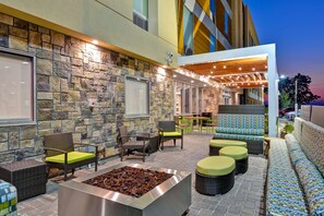An outdoor patio with stone walls, wicker furniture, a fire pit, and string lights. - Home2 Suites by Hilton Hot Springs (Hot Springs)