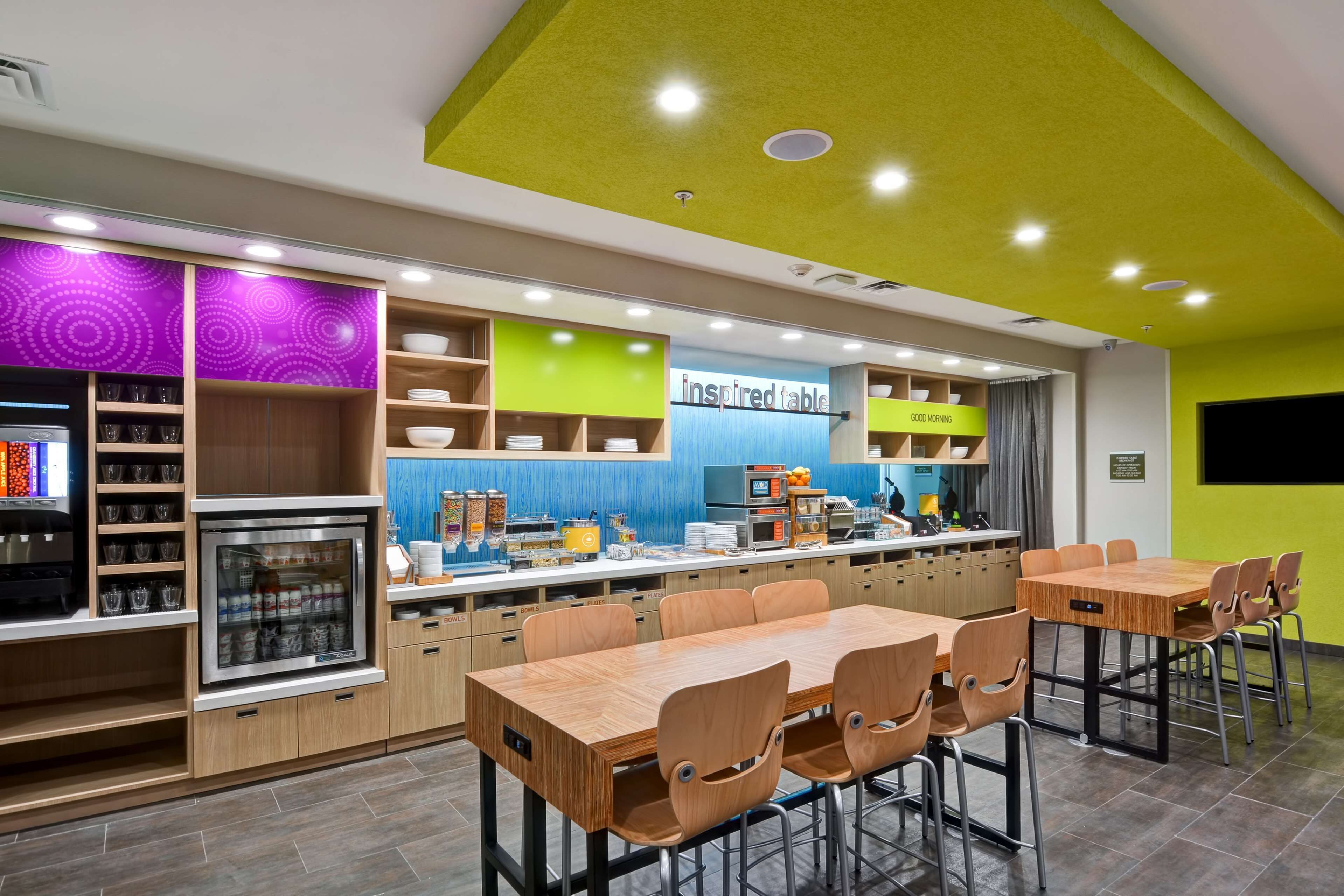 Un restaurante moderno con un techo amarillo brillante, una barra con un letrero que dice 'Good Morning' y una zona de estar con mesas y sillas de madera.