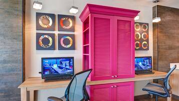 A modern office space with a pink cabinet, two desks with computers, and wall-mounted monitors displaying a virtual tour.