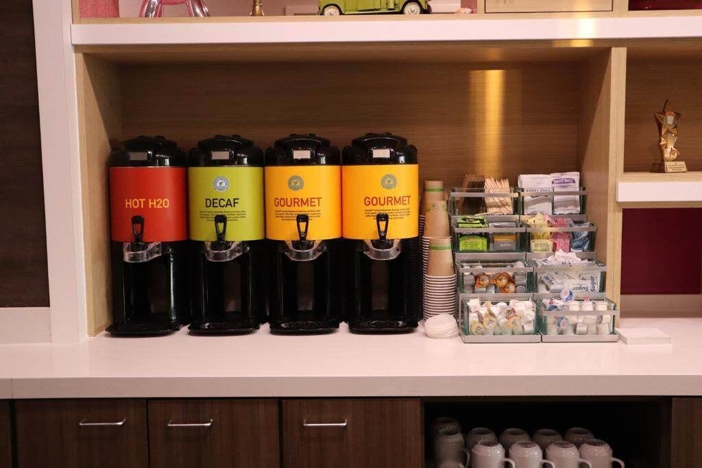 Un espace dédié au café, équipé de quatre distributeurs étiquetés « EAU CHAUDE », « DÉCAFÉINÉ » et « GOURMET ».