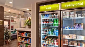 Un hall d’hôtel comprenant un distributeur automatique rempli de boissons et d’en-cas, un comptoir de réception et un panneau indiquant l’emplacement de l’ascenseur.