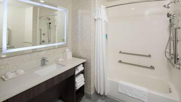 A modern bathroom with a large mirror, dual sinks, a shower with grab bars, and a towel rack.