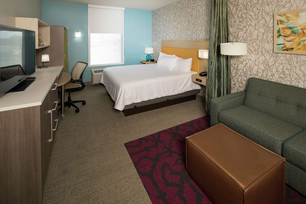 A hotel room with a bed, a desk with a computer, a chair, a sofa, and a small table.