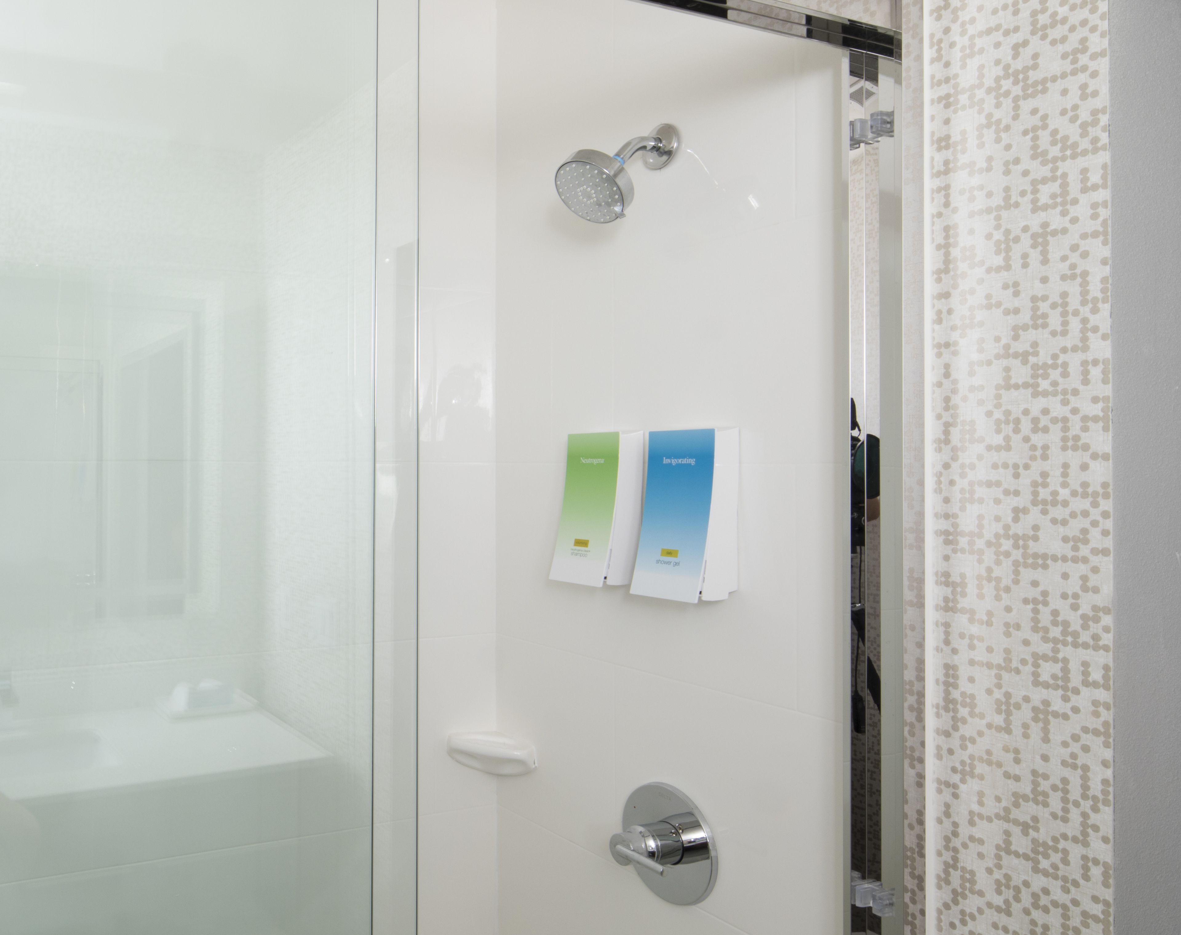 A modern bathroom with a glass shower enclosure, a handheld showerhead, and a towel rack with two folded towels.