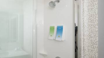 Un baño moderno con cabina de ducha de vidrio, ducha de mano y toallero con dos toallas dobladas.
