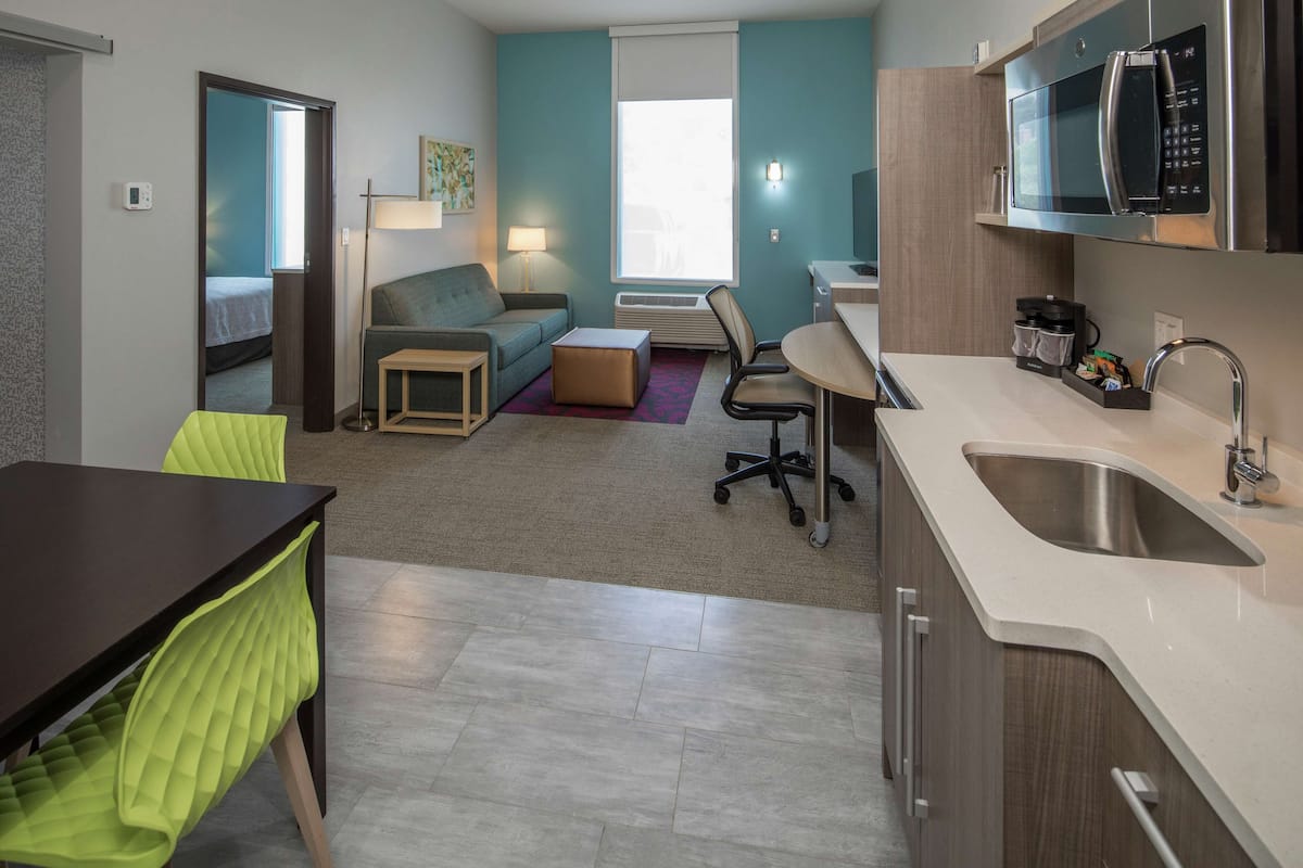 A compact hotel room with a kitchenette, a sofa, a dining table, and a small office area.