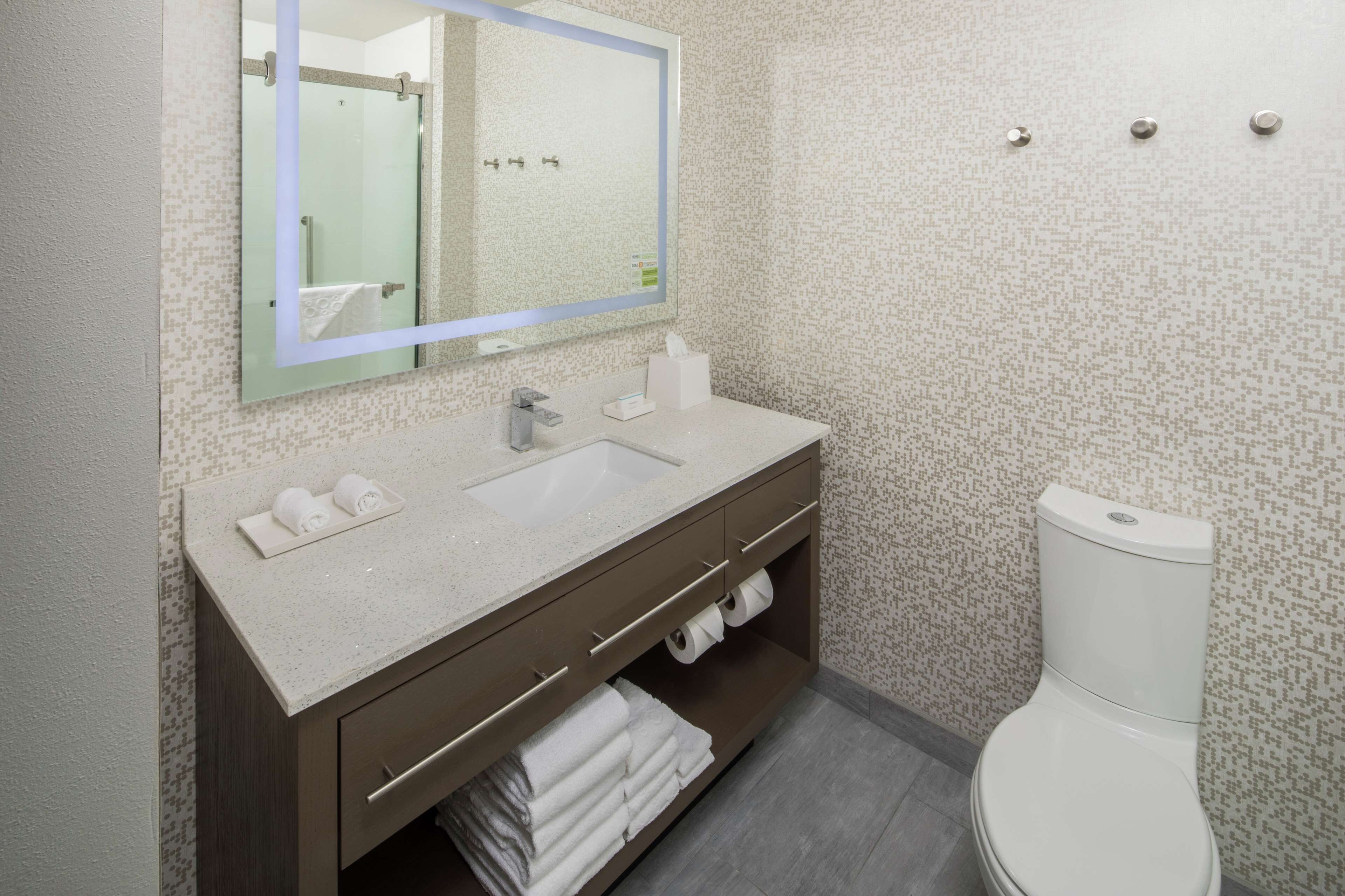 Un baño moderno con un espejo grande, un lavamanos, un inodoro y un perchero para toallas.